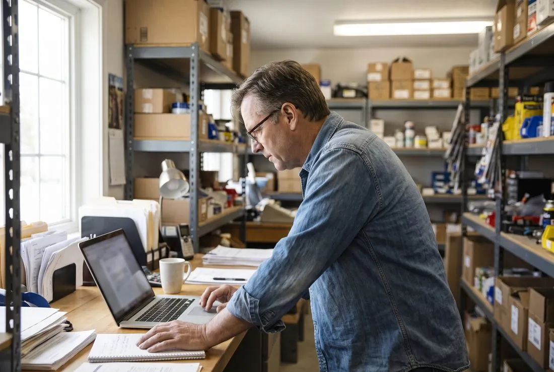 A shop owner at a laptop in the back office of his store